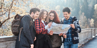 Group of young people are looking at the map where they are while walking in autumn forest.